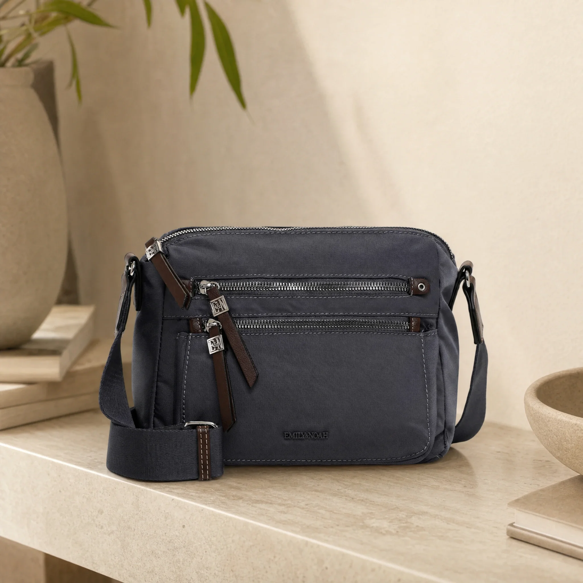Sfeerbeeld: grijze crossbody-tas met ritsvakken op een lichte stenen tafel