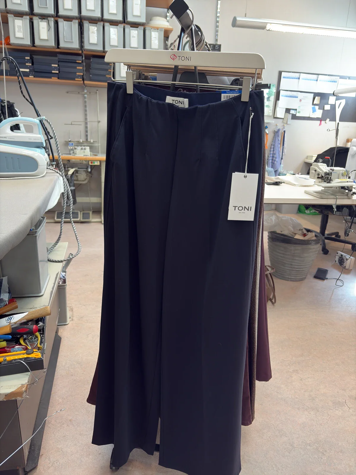 Marineblauwe pantalon aan een kledingrek in het atelier, gefotografeerd met een telefoon