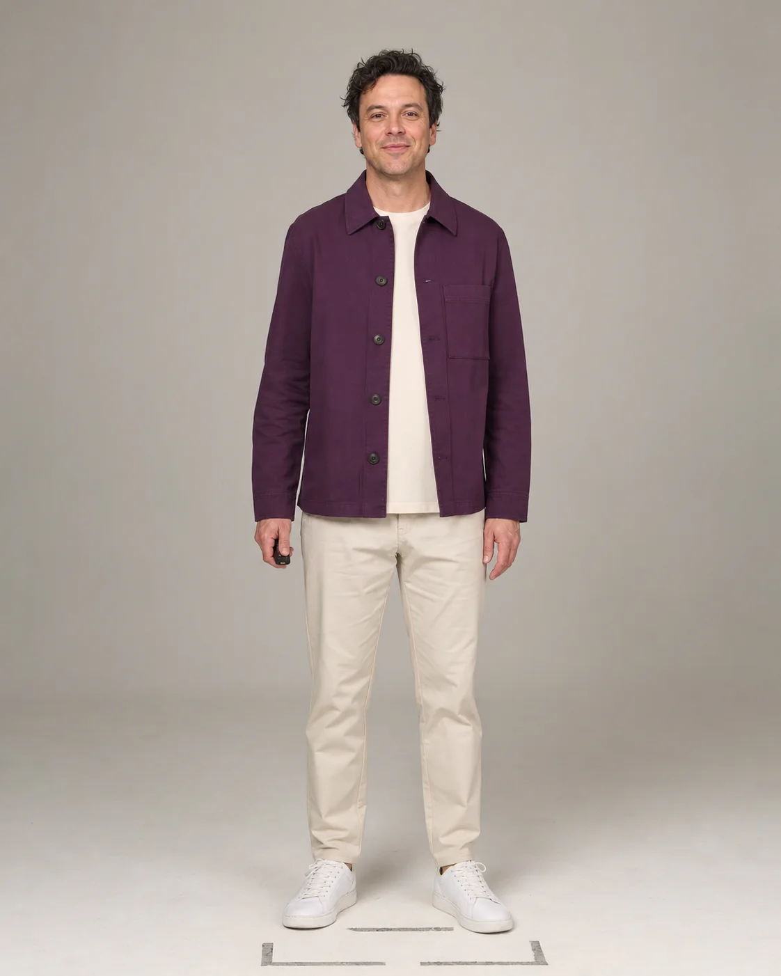 Opname in een studio van een man in een paarse overshirt en lichte chino, met afstandsbediening in de hand