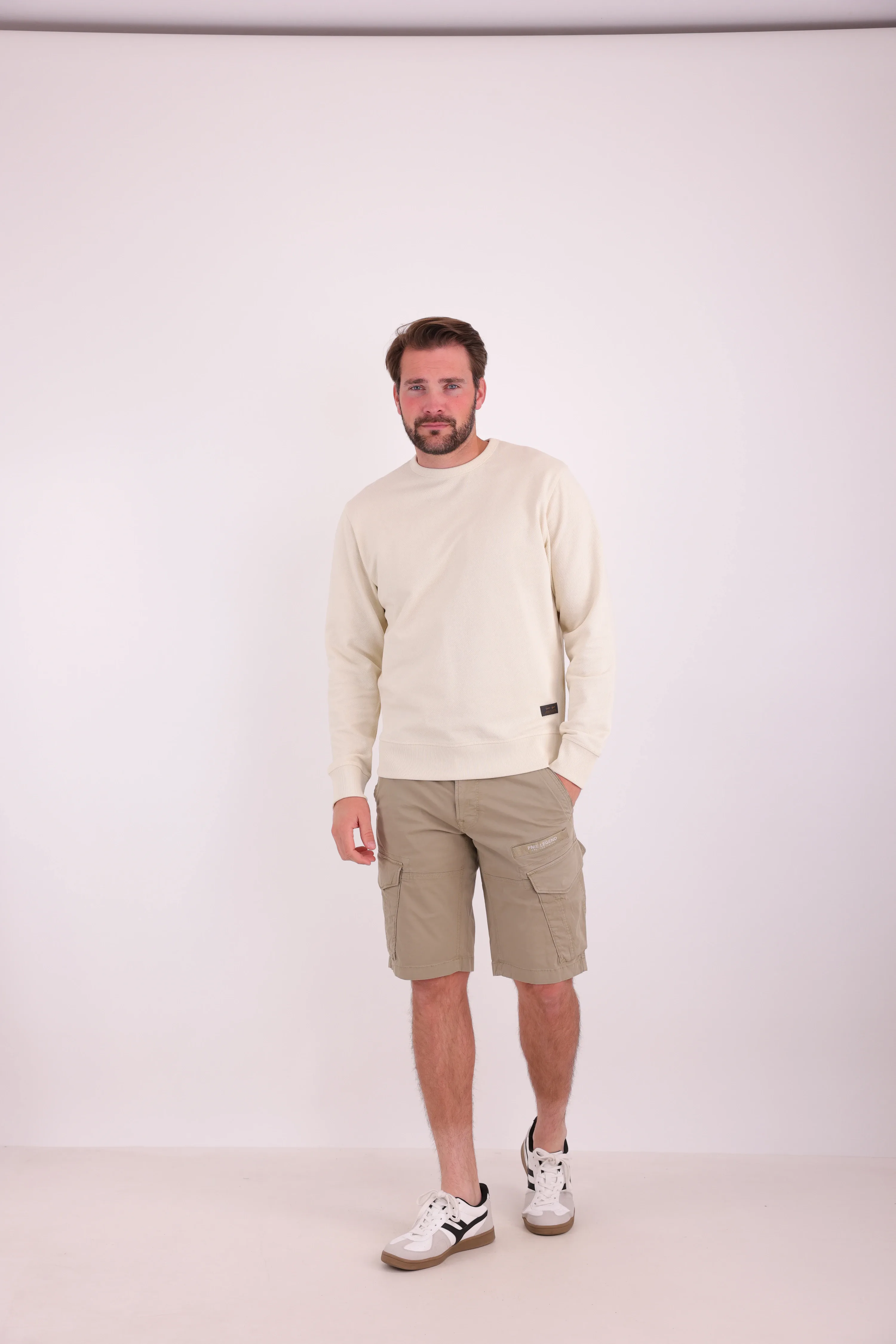 Studiofoto van een model in een crèmekleurige sweater en een beige cargoshort