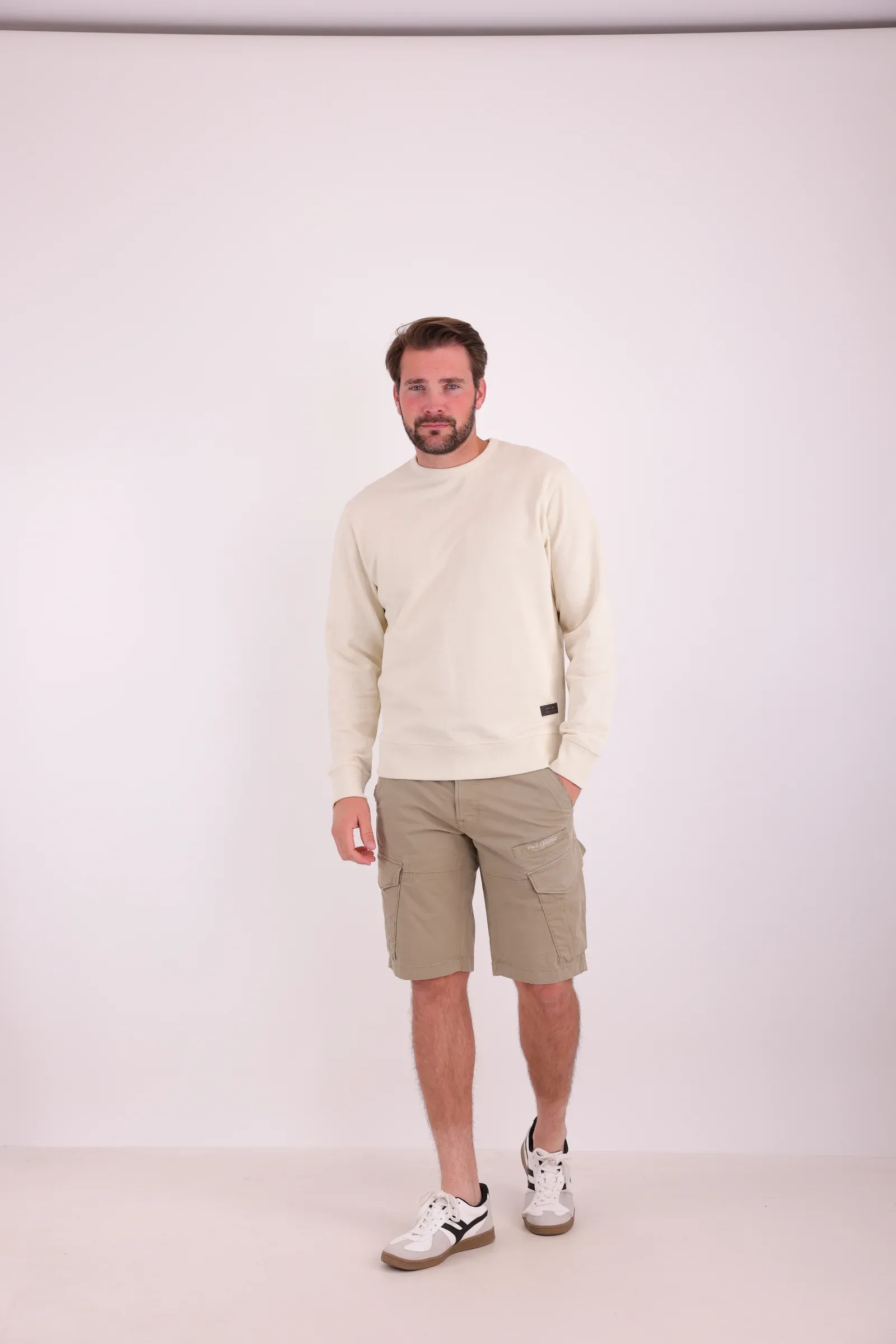 Studiofoto van een model in een crèmekleurige sweater en een beige cargoshort
